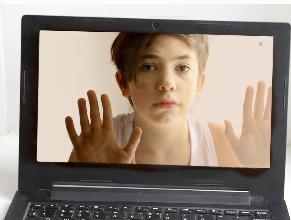 Young boy addicted to computer and the internet looking out from inside computer screen