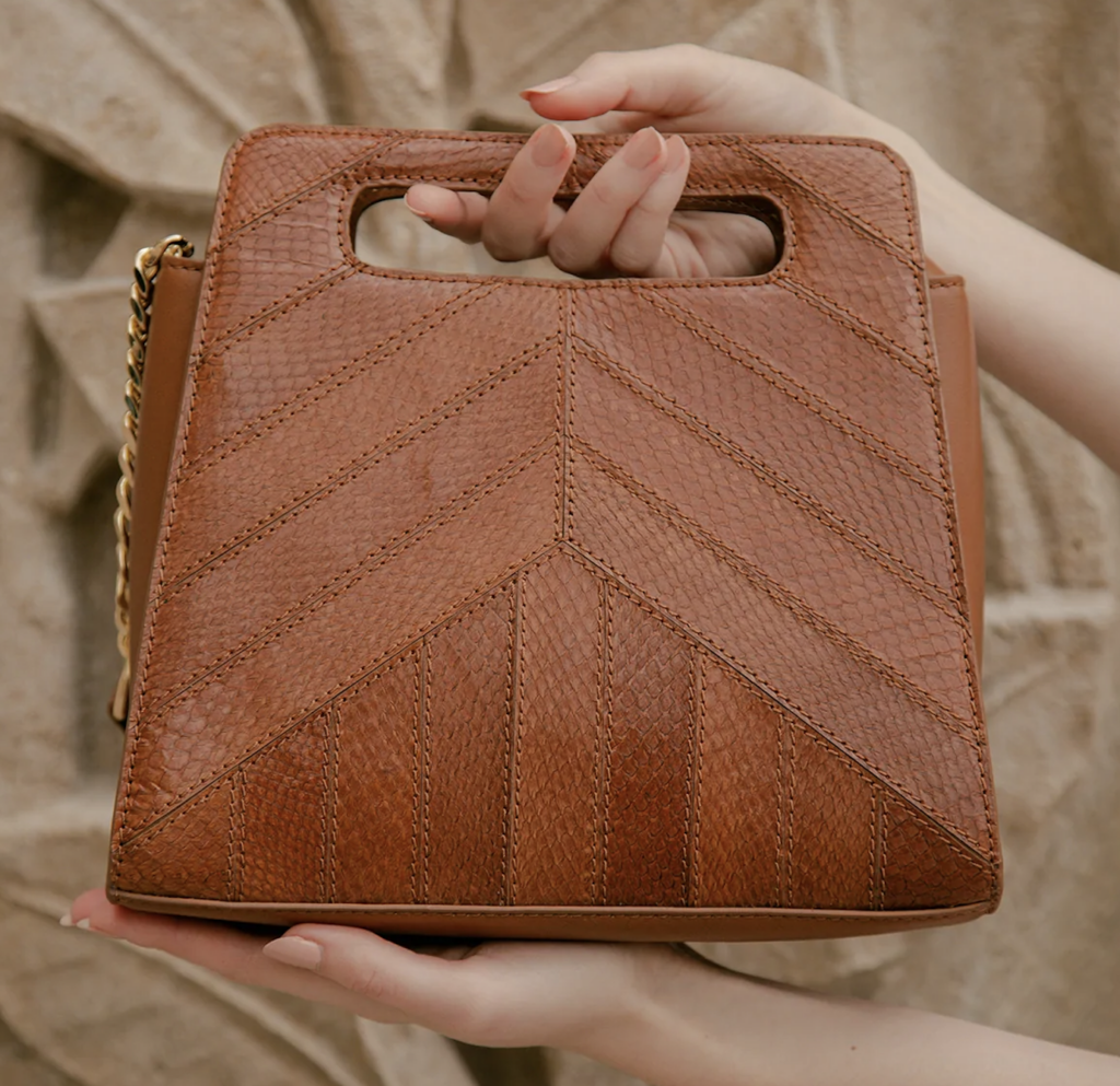 Beautiful tan handbag with pattern stitching being held by female hand