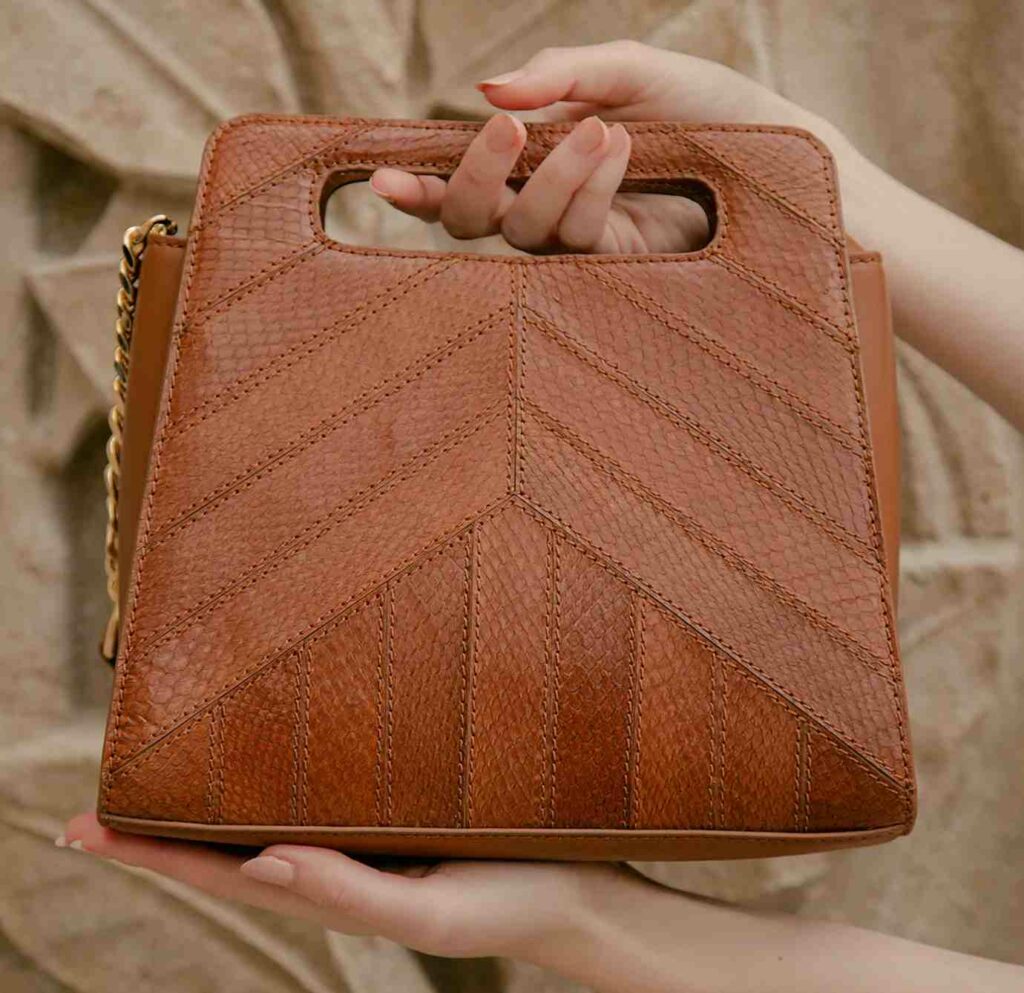 Beautiful tan handbag with pattern stitching being held by female hand  