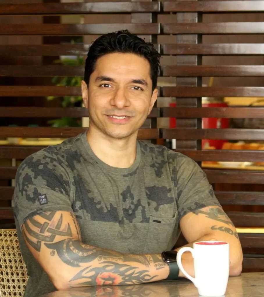 Luke Coutinho - a prediabetes and diabetes coach - sitting with a cup at a table smiling