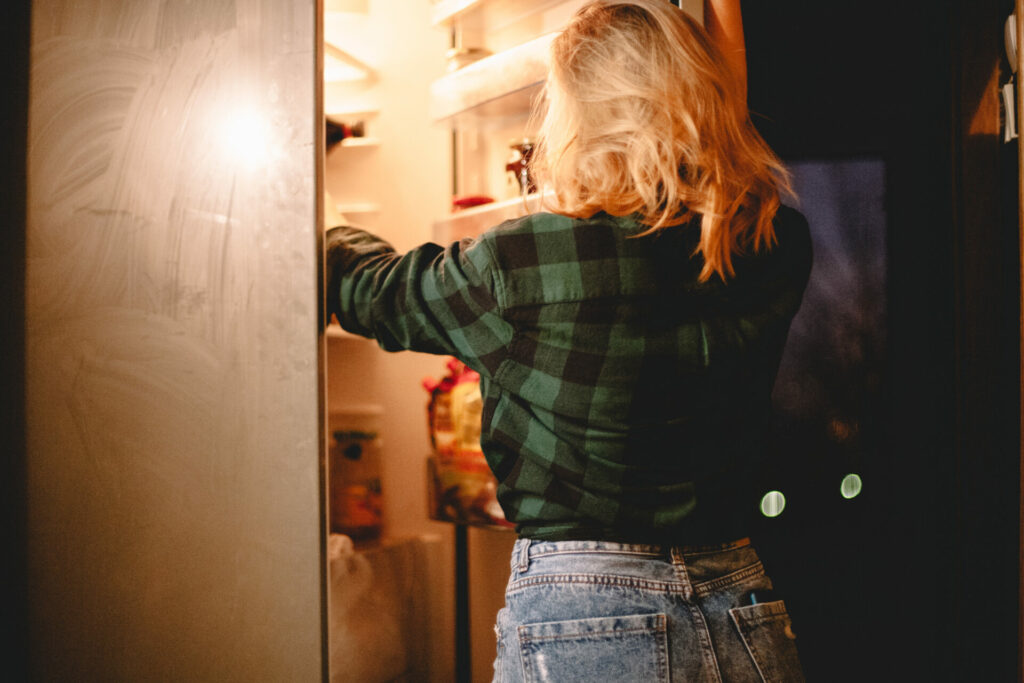 Blonde woman reaching for food in the fridge at night 