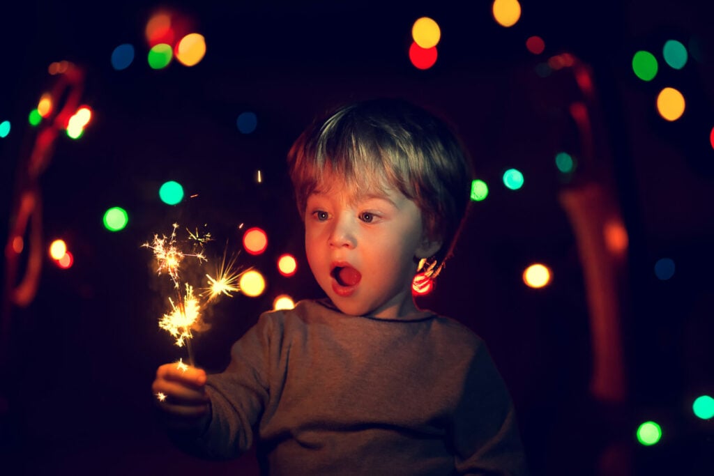 young blonde boy holding a sparkler with mouth open in awe