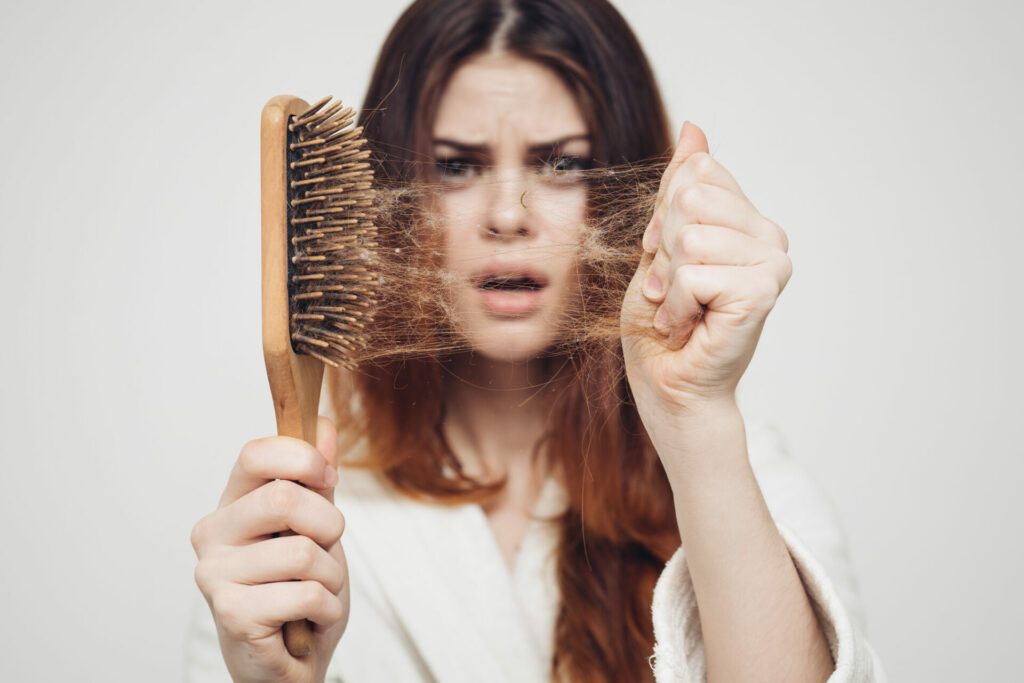 woman looking horrified while pulling lots of hair from a hairbrush 