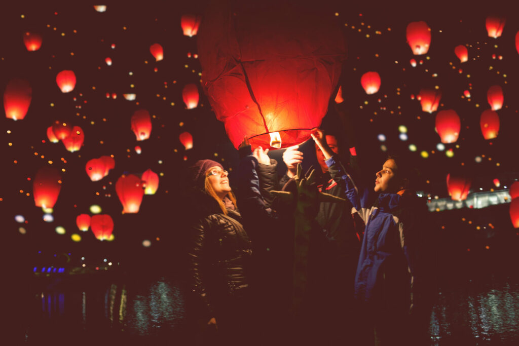 family lighting a sky lantern on bonfire night with many red lanterns already floating in the sky