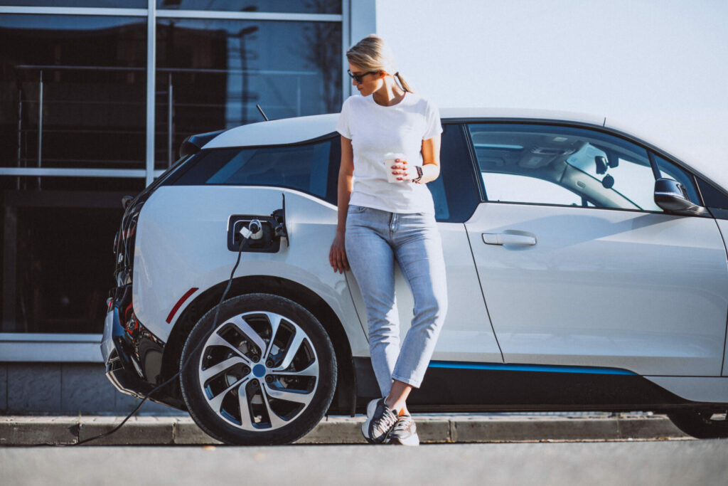 Woman drinking coffee standing next to electric car as it charges