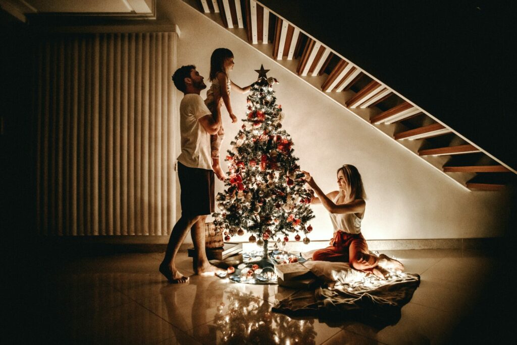 man woman and child decorating brightly lit tree in the dark