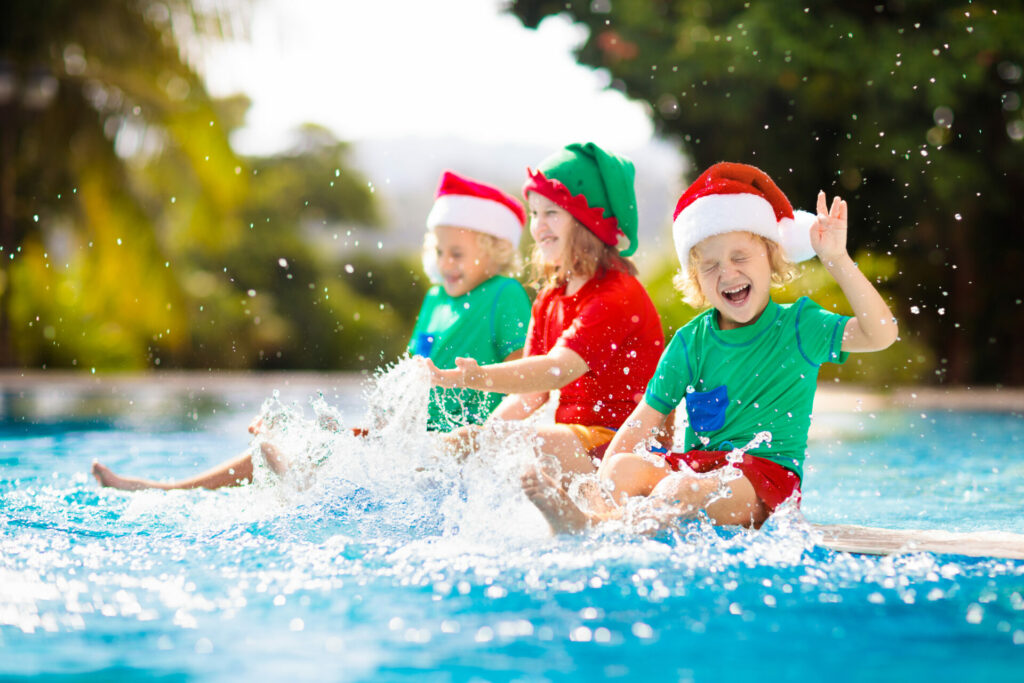 Kids in santa hats splashing their feet in a swimming pool 