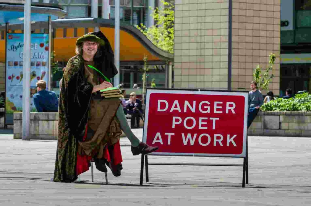 Martin Kiszko seated next to a sign tyhat reads 'danger poet at work' in fancy dress
