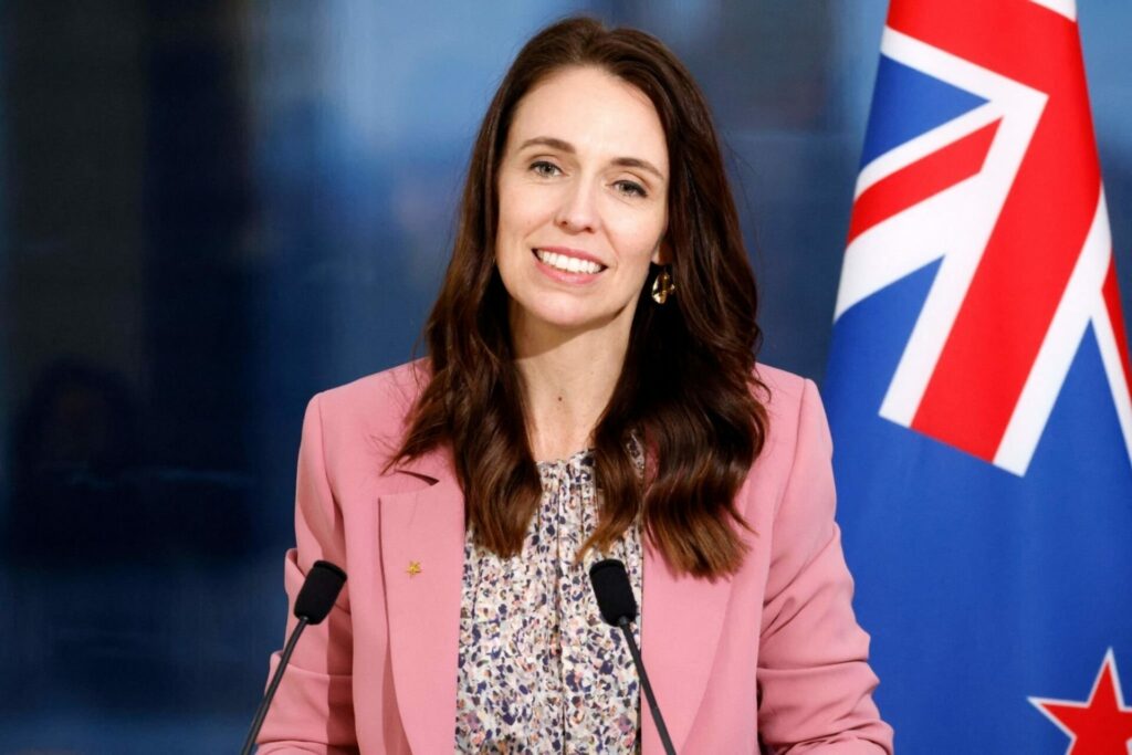 Jacinda Ardern in pink jacket next to New Zealand flag before she quit as prime minister