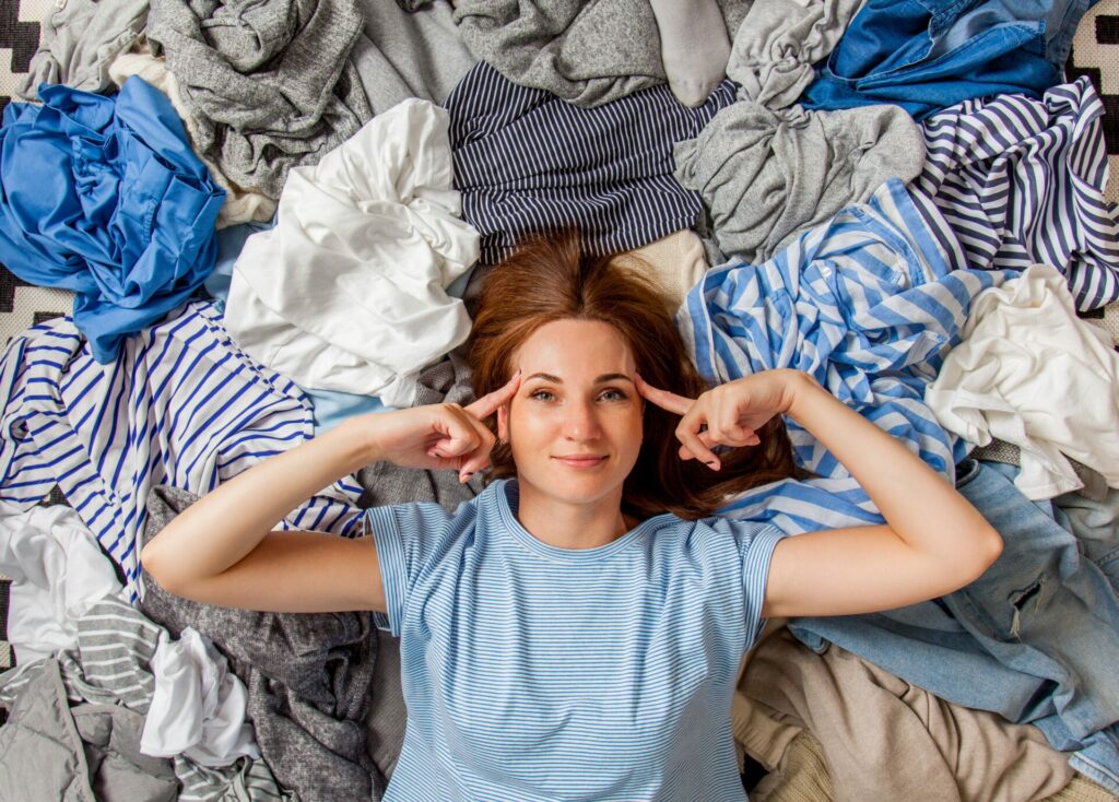 woman lying on lots of clothes getting ready to declutter