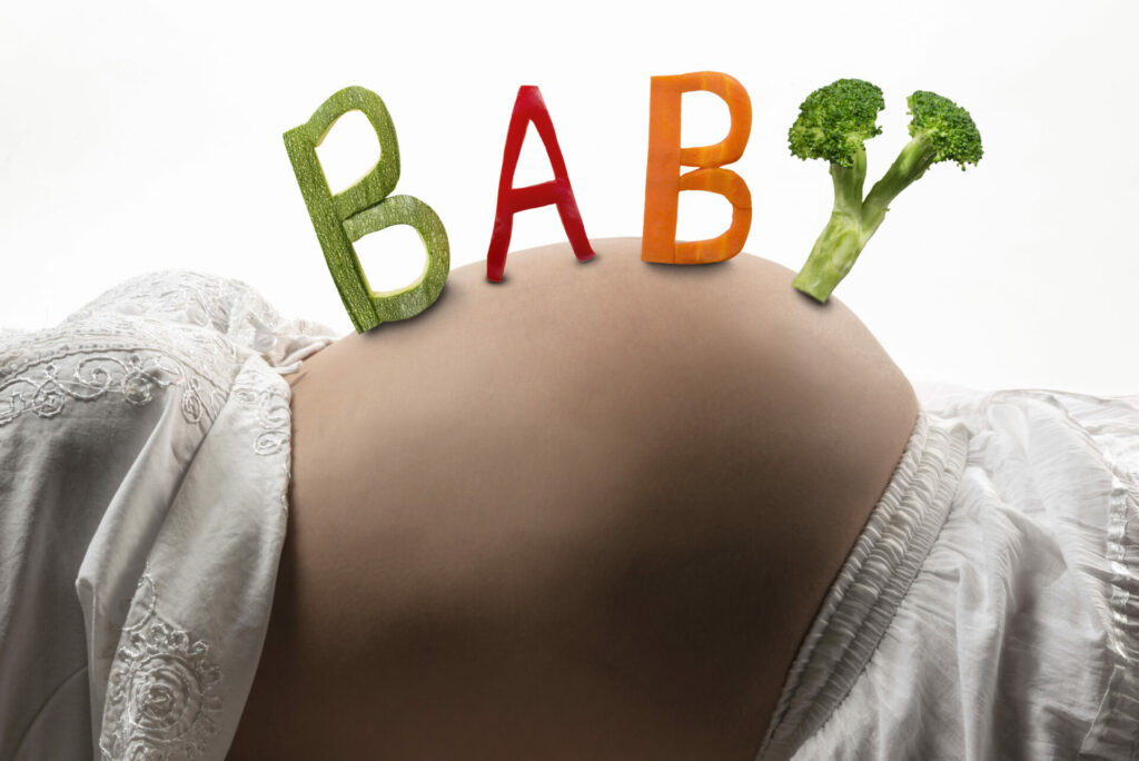 baby spelled out on pregnancy bump with vegetables: concept of fertility diet 