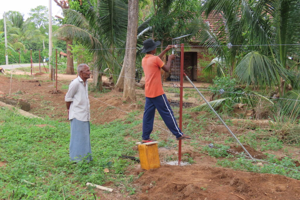 villagers building electric fencing to keep elephants from destroying their crops and houses 