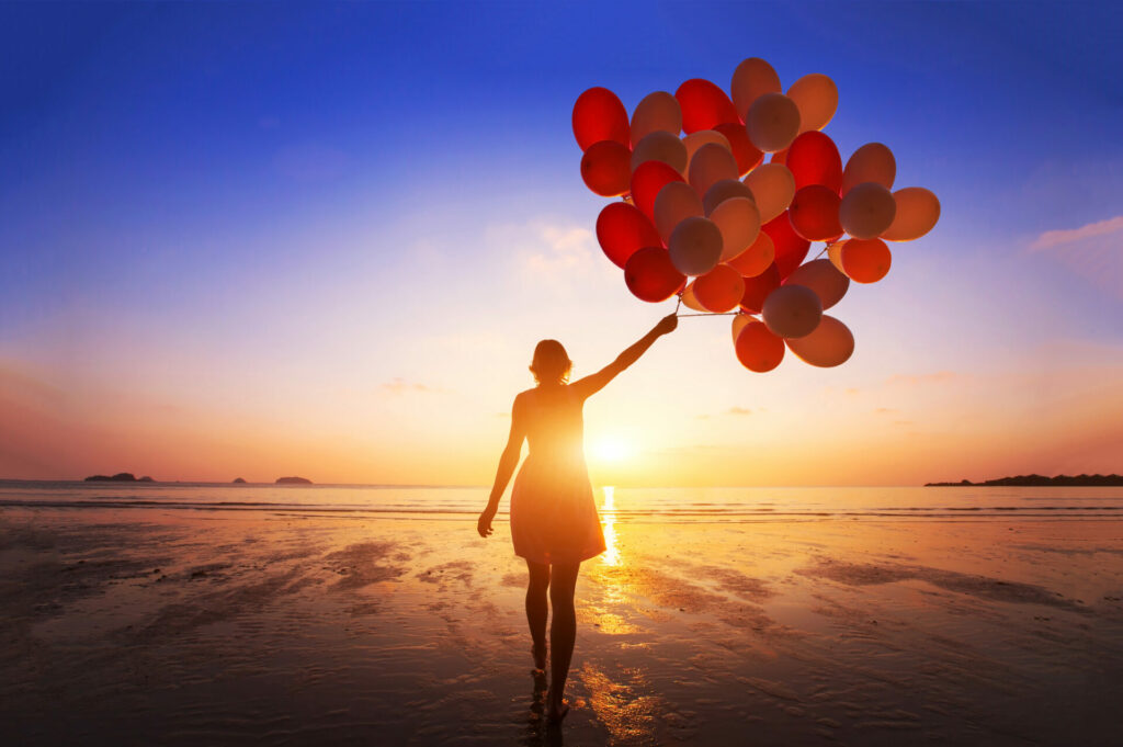 girl on beach with balloons being happy after manifesting her happy life 