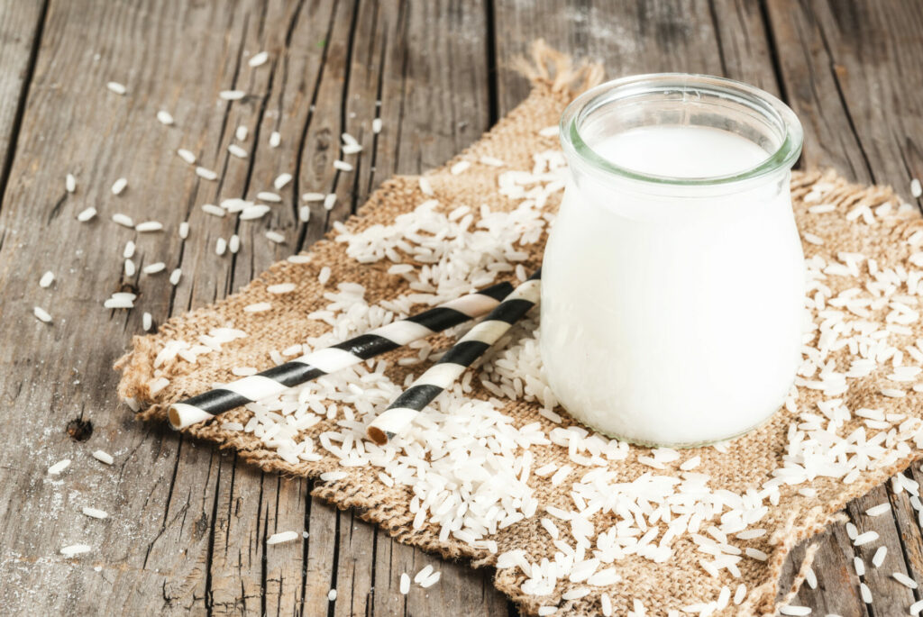 Rice milk, with rice grains. On a rustic wooden table. With a striped tube for drinking. Copy space