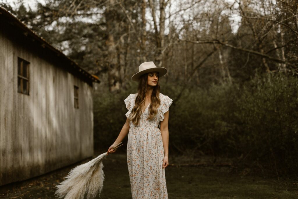 woman wearing pretty floral dress and holding dry grass with hat on 