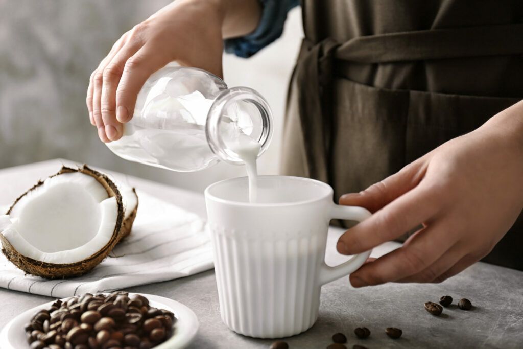 coconut as a plant-based milk being poured into a cup with coffee beans nearby 