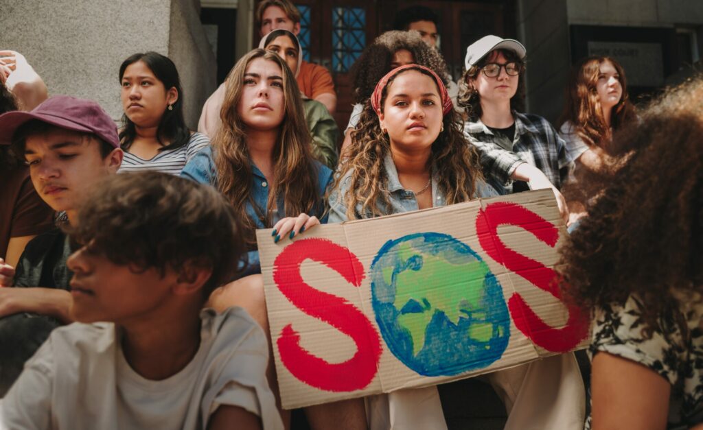 Gen Z - two young women/teenagers in group holding up sign that says SOS but the O is planet earth