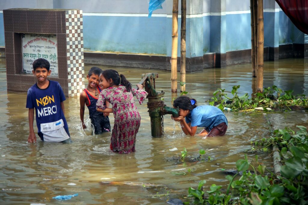 children in flood water drinking fresh water at a tap 