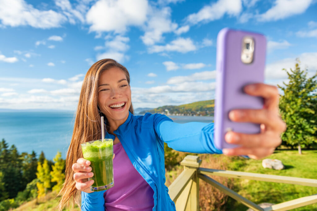 influencer holding a green smoothie with sea behind her 