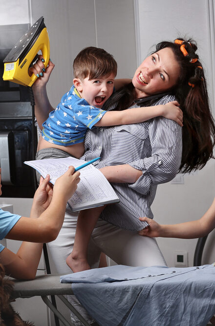 very busy mum doing ironing while helping three kids with homework and games