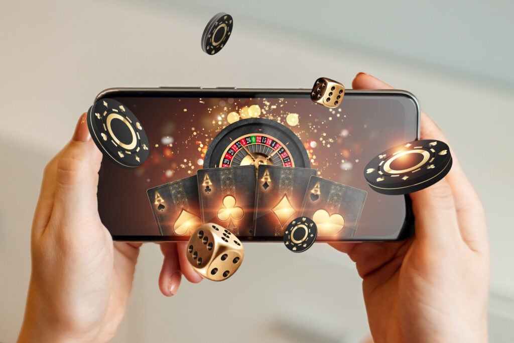 A woman's hand holding smartphone with playing cards, roulette and chips
