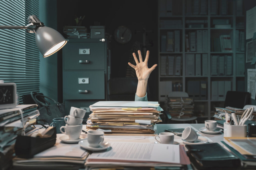 Hand reaching out from paperwork mountain