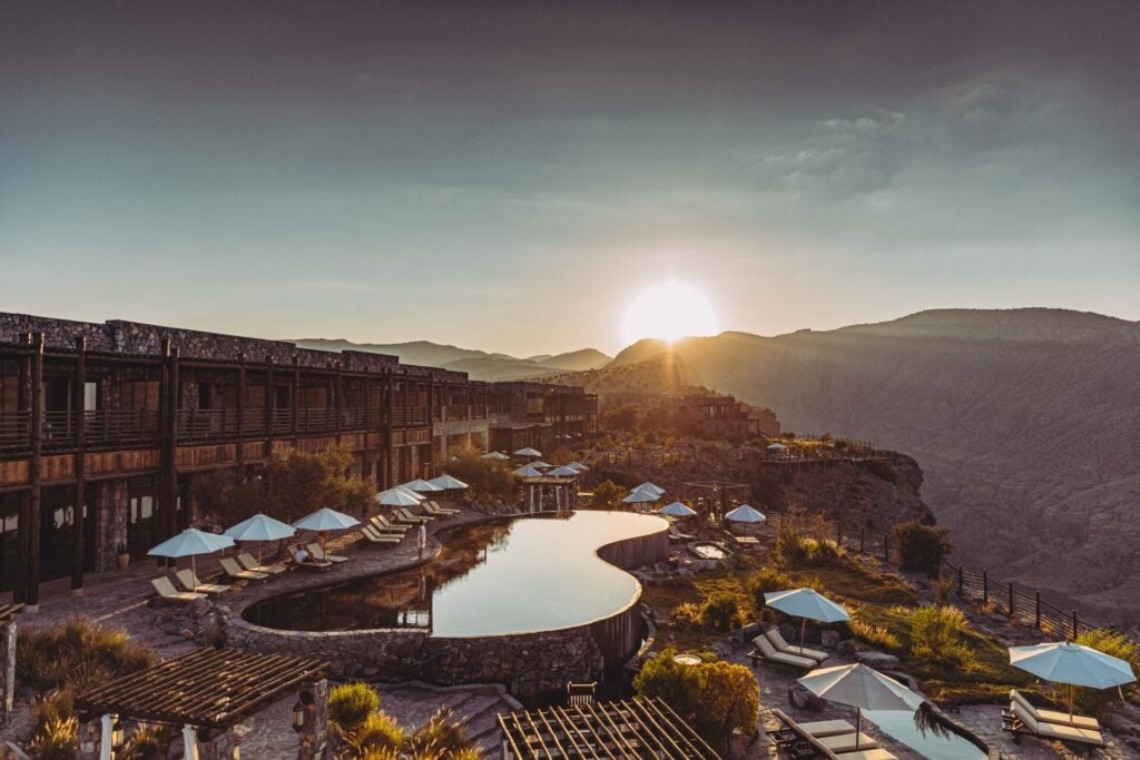a pool with umbrellas and a building in the background at Alila Jabal Akhdar
