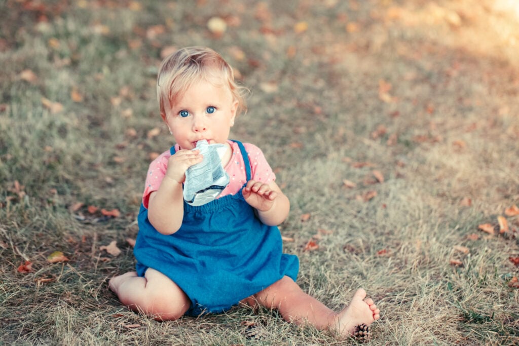 toddler with food pouch sat on the grass