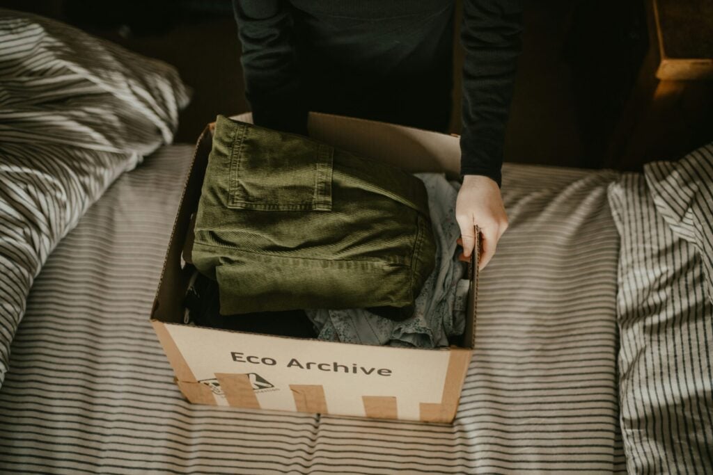 Person packing clothes into a cardboard box labeled Eco Archive as one of the top moving tips 
