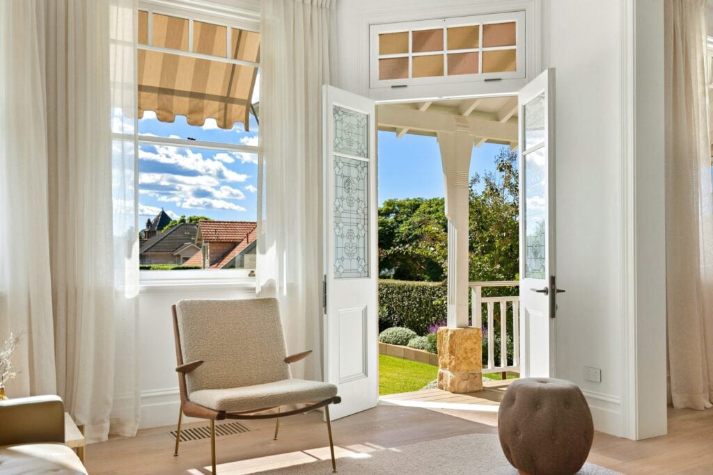 a room with a chair and a french doors looking out onto a pergola balcony and garden with blue sky 