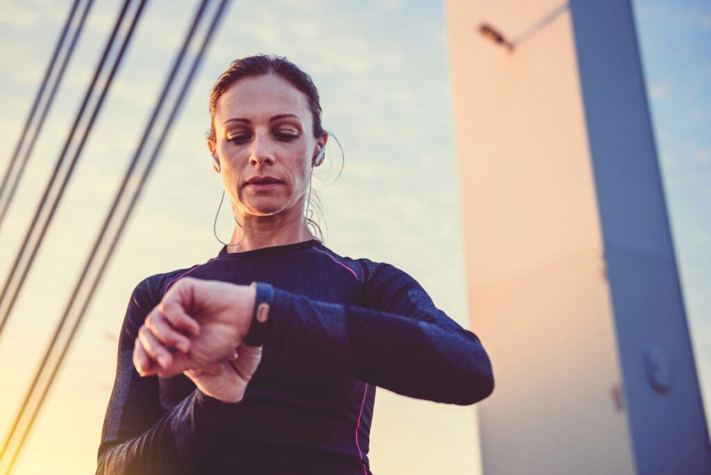 a woman looking at her smart watch on a run with headphones in 