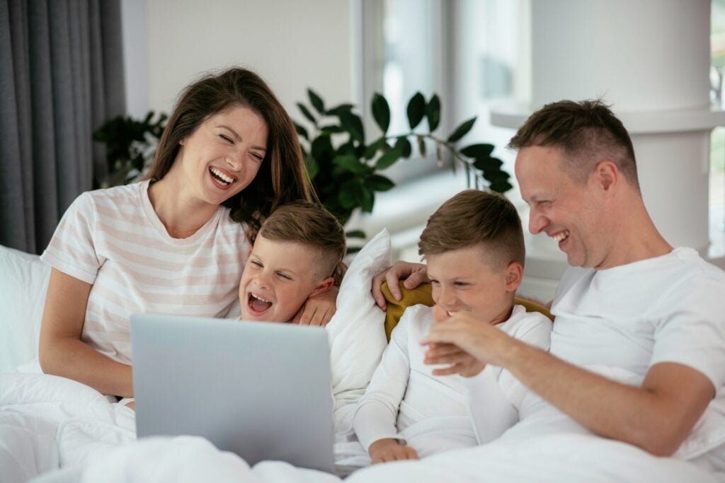 a family sitting on a bed looking at a laptop