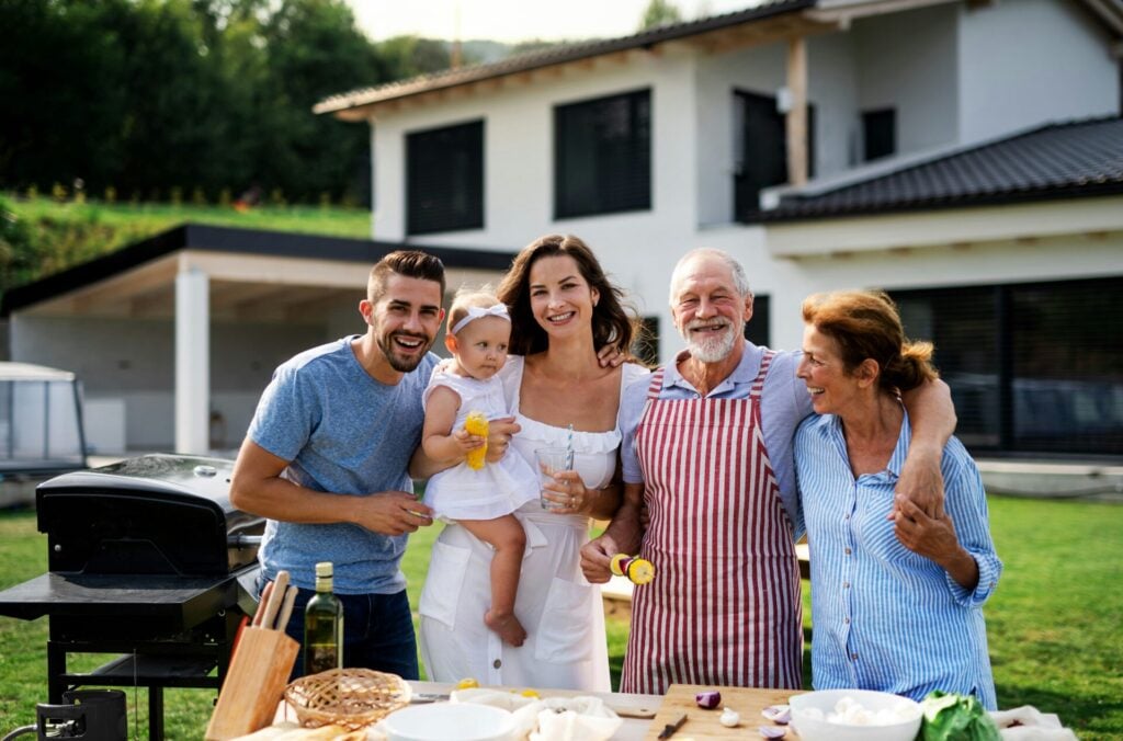 a group of people standing around a table with food with elderly parents in garden having a bbq