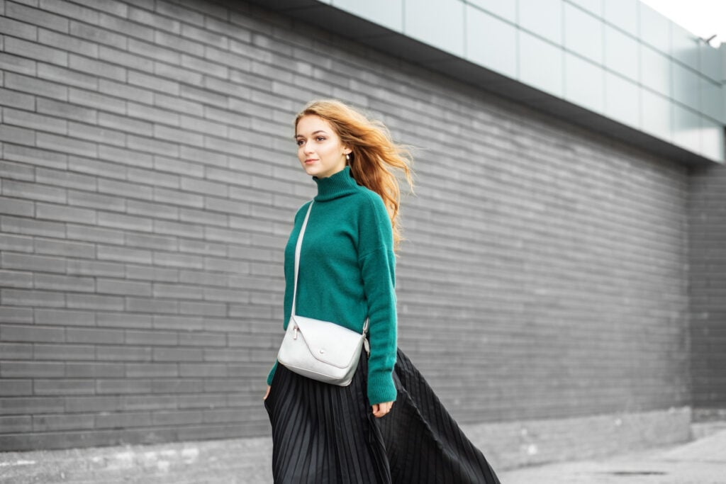 A beautiful tall woman walks in a long skirt and a green sweater. Small women's handbag.