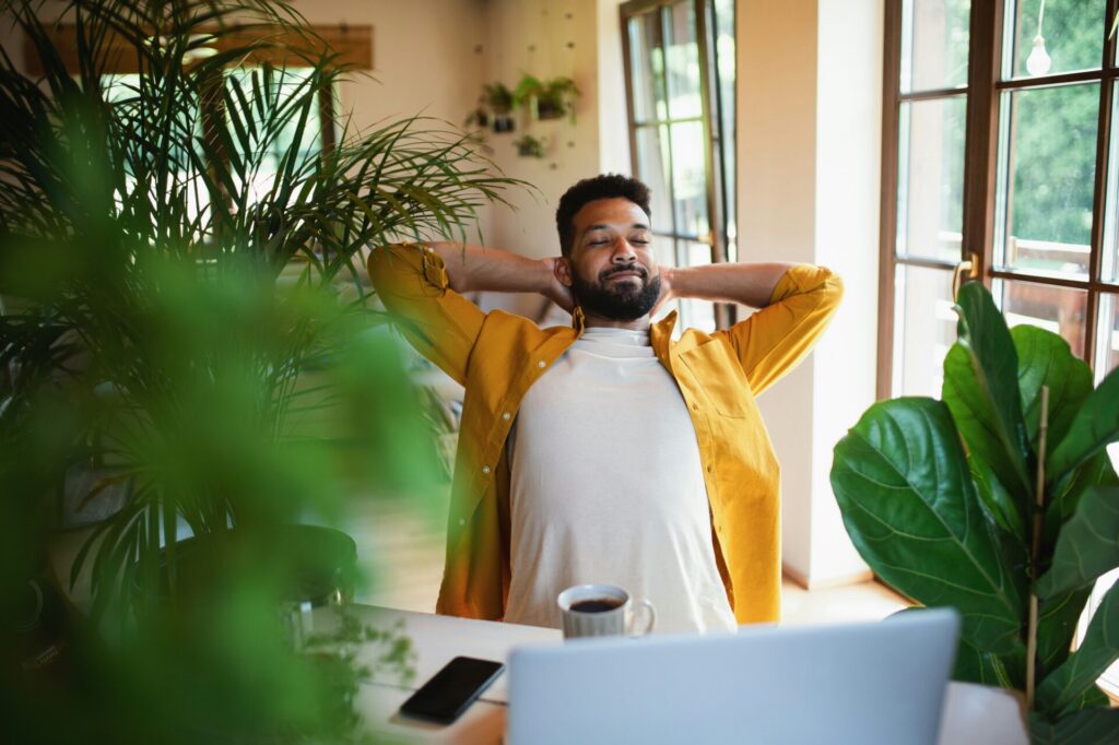 remote worker at home, surrounded by indoor plants with a coffee cup at his side 