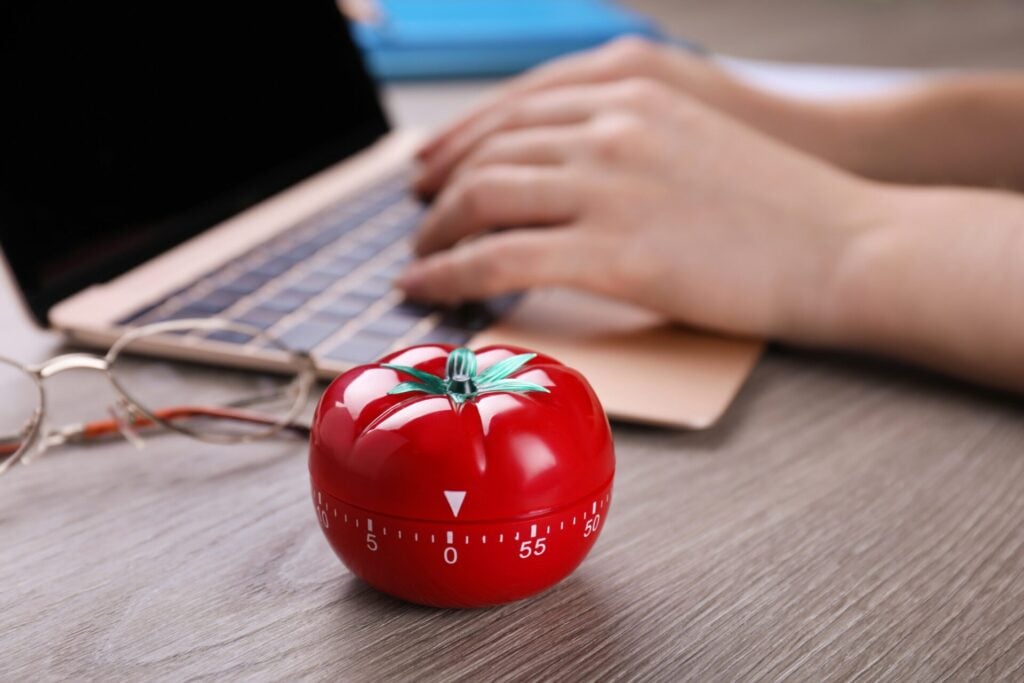 A pomodoro timer next to a desk with woman's hand working 