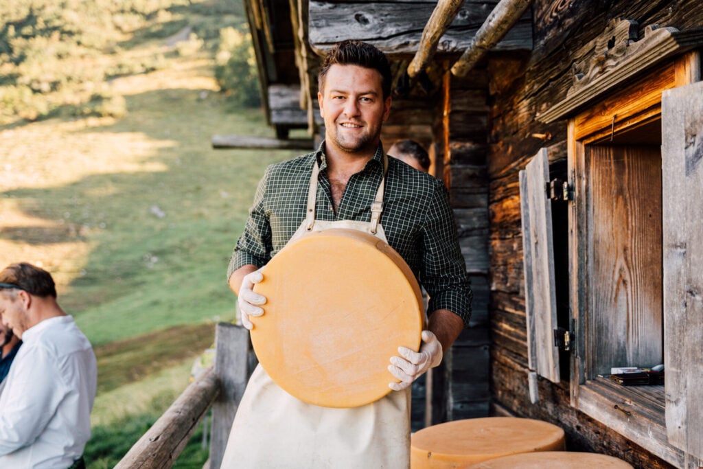 Man holding cheese wheel outdoors.