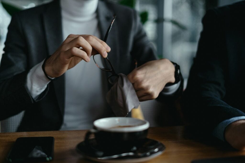 Man cleaning eyeglasses near coffee