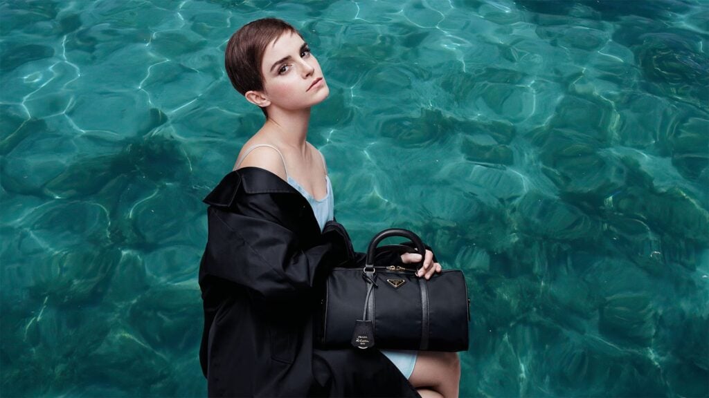 Emma Watson holding black handbag by water in sustainable fashion campaign for Prada