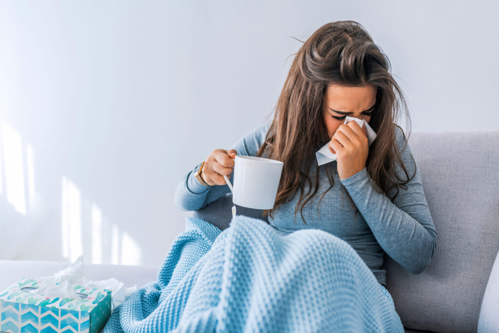 Woman with coffee and tissues sneezing with allergies 