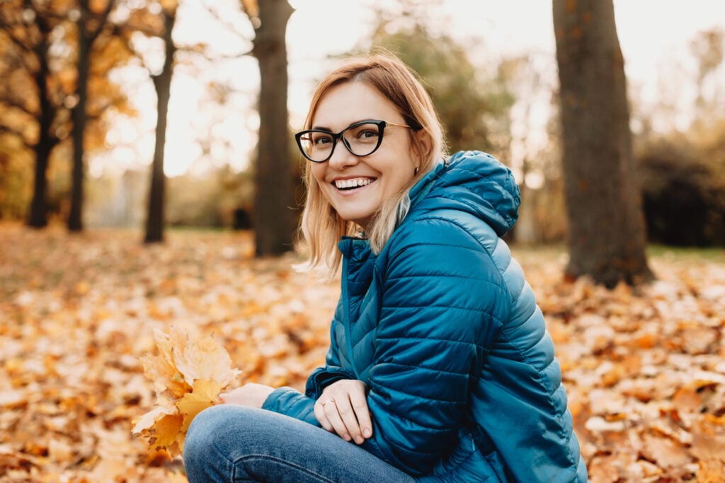 Woman sitting in autumn leaves wearing black eyeglasses