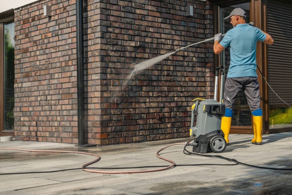 Person pressure washing a brick wall