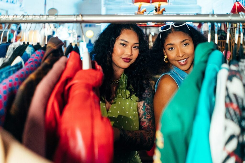 Two people browsing colorful preloved clothing racks.