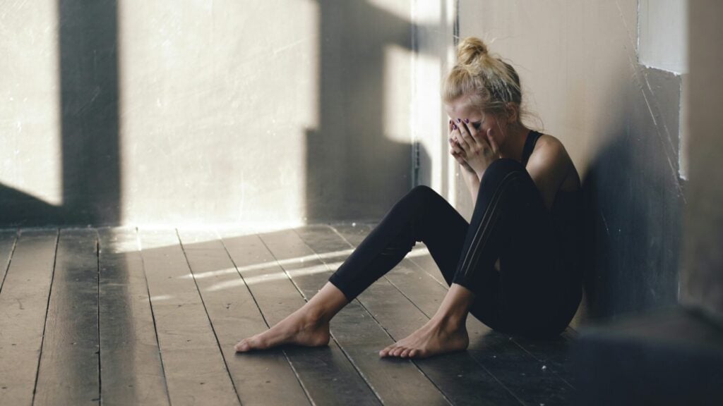 Person sitting alone in shadows crying over hair loss - showing stress and too thin