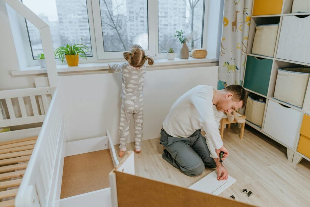 Parent assembling kids furniture with child nearby.
