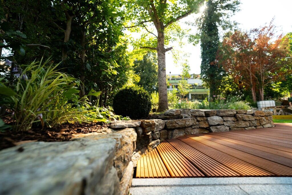 Lush garden with wooden decking and stones.