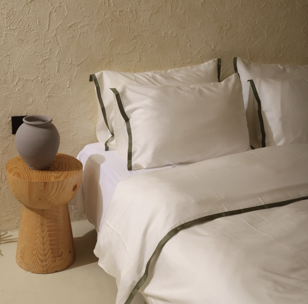 soft bedding with green trim with wooden stool and vase nearby