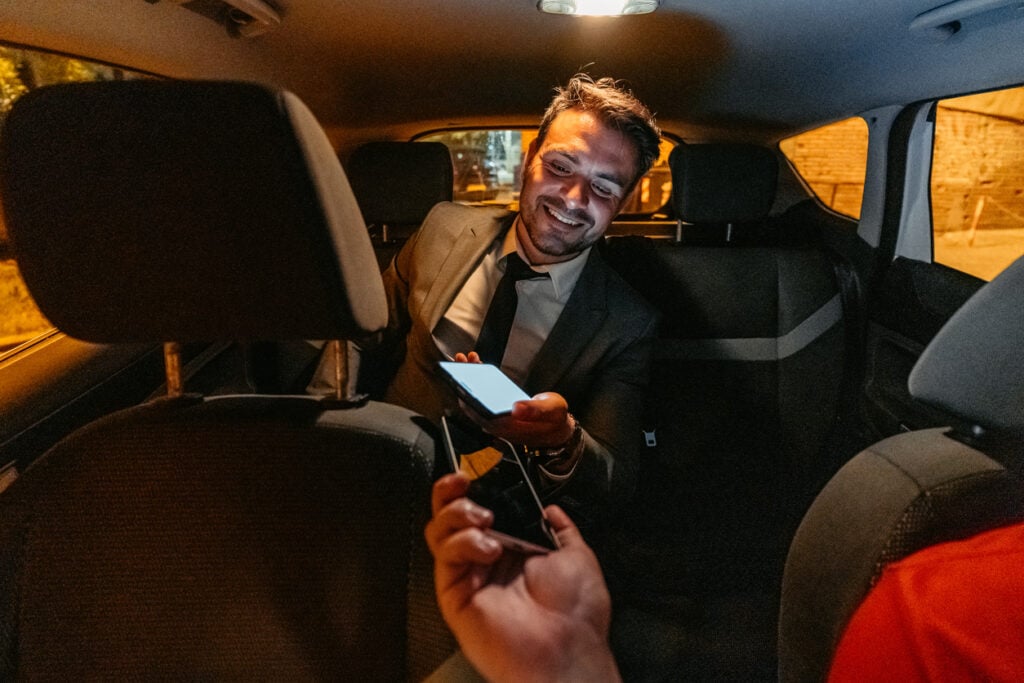 Mid-adult businessman paying his taxi driver by mobile banking application at night.