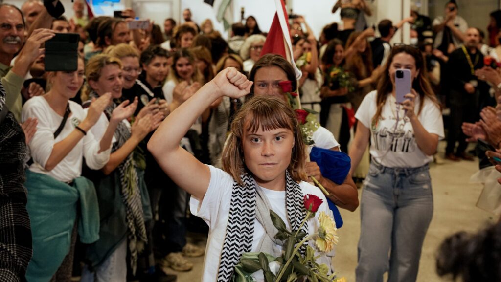 Greta Thunberg at the airport arrivals carrying flowers with  a victory sign 
