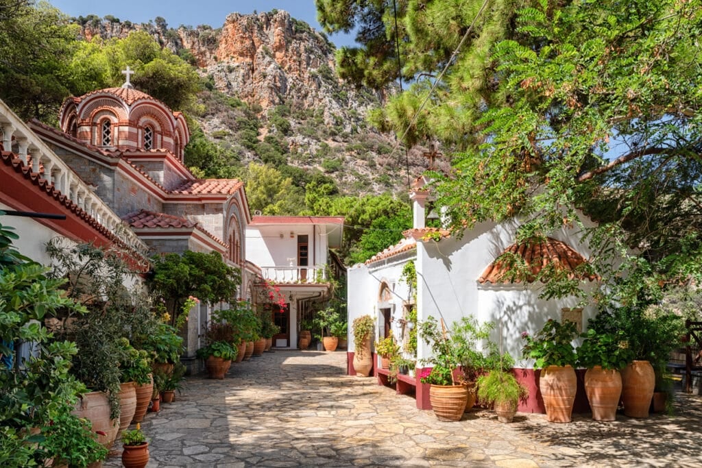 Monastery of Saint George, Crete, Greece – September 2, 2025: Scenic view of traditional Greek Orthodox monastery courtyard with stone path, potted plants and surrounding mountains.